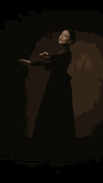 a woman in a black dress is standing with her arms outstretched .