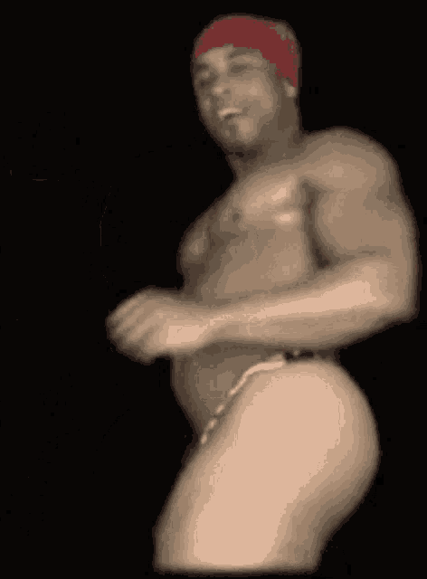 a shirtless man with a red bandana on his head is dancing in the dark .