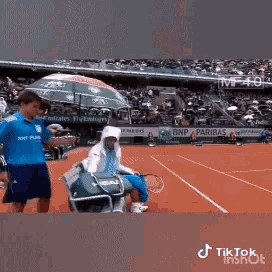 a man in a blue shirt is standing next to a man in a wheelchair on a tennis court
