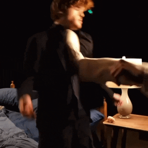 a man in a suit is dancing in front of a lamp in a bedroom .
