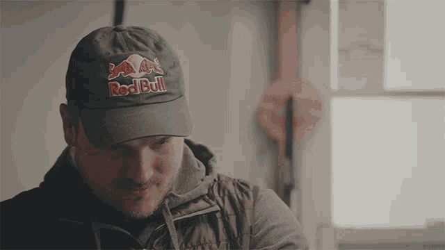 a man wearing a red bull hat is looking down