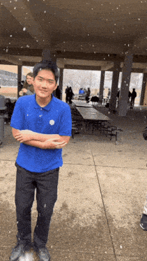 a man in a blue shirt with a badge on his chest stands in the snow with his arms crossed