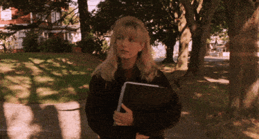 a woman walking down a sidewalk with a book in her hand