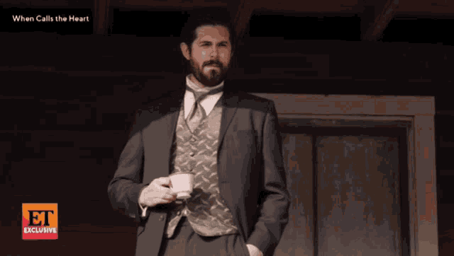 a man in a suit is holding a cup of coffee in front of a sign that says et exclusive