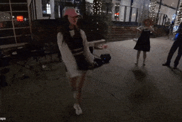 a woman in a pink hat is dancing in front of a building that has a red sign that says exit