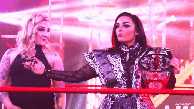 two women are standing in a wrestling ring and one is holding a championship
