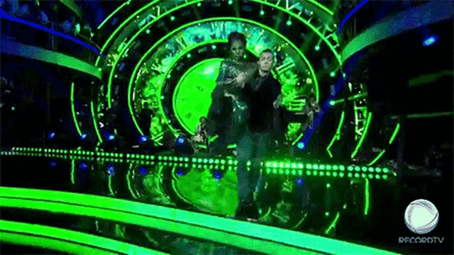 a man and a woman are dancing on a stage with a green background .