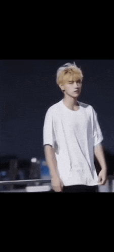 a young man with blonde hair is wearing a white t-shirt and standing in front of a black background .