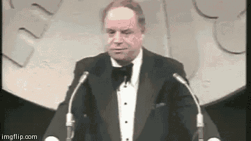a man in a tuxedo is standing at a podium giving a speech .
