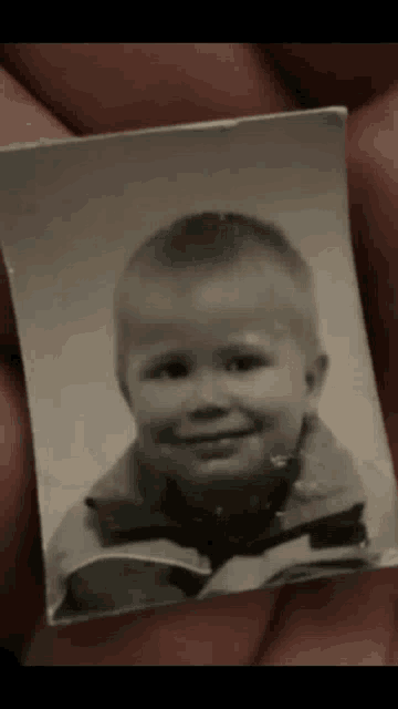 a person is holding a black and white photo of a young boy .
