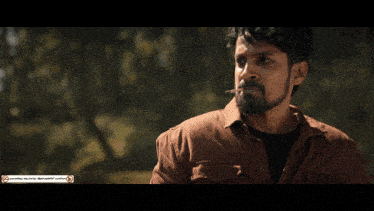 a man in a brown shirt is smoking a cigarette in a forest