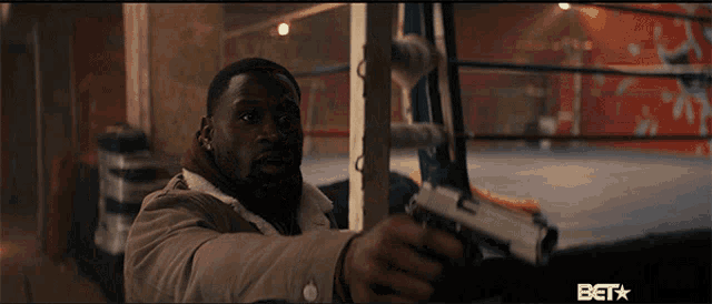 a man holding a gun in a boxing ring with a bet logo on the bottom