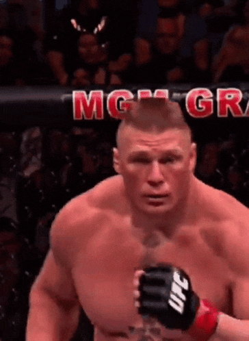 a shirtless fighter wearing a ufc glove is standing in front of a crowd .