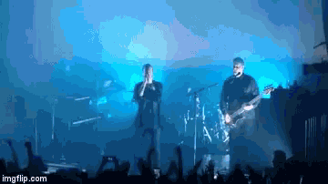a man singing into a microphone while another man plays a guitar in front of a crowd at a concert