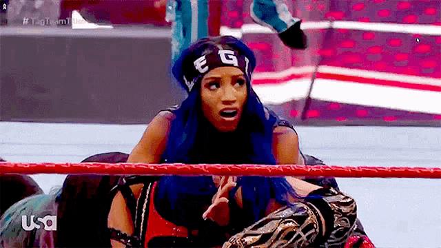 a woman with blue hair and a headband that says e and g is sitting in a wrestling ring .