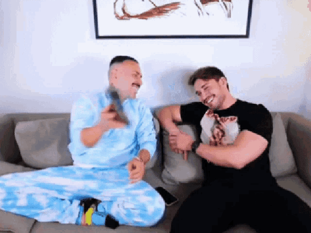 two men are sitting on a couch with one wearing a t-shirt that says ' jesus '