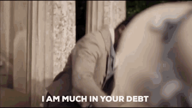 a man in a suit is saying `` i am much in your debt '' while standing in front of a building .