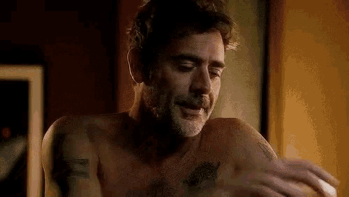 a shirtless man with a tattoo on his chest is smiling and looking at the camera .