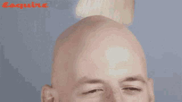 a bald man with his eyes closed is being shaved by an esquire magazine