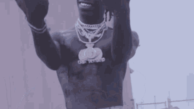 a man without a shirt is giving the middle finger while wearing a necklace with a dollar sign on it .