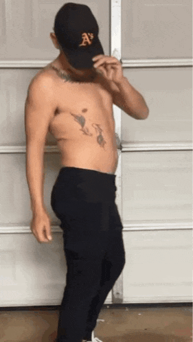 a shirtless man is standing in front of a garage door wearing a hat .