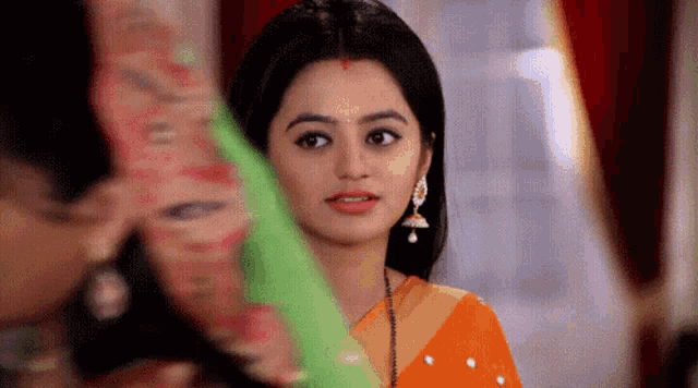 a woman in an orange saree and earrings is looking at the camera .