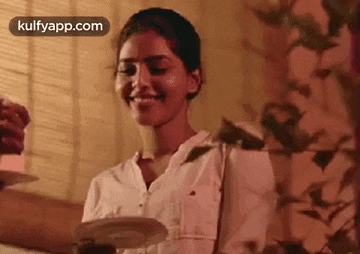 a woman is smiling while holding a plate of food in her hand .