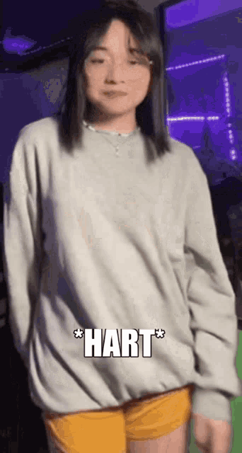 a woman wearing a grey sweater and yellow shorts is standing in front of a green screen with the word hart on it .