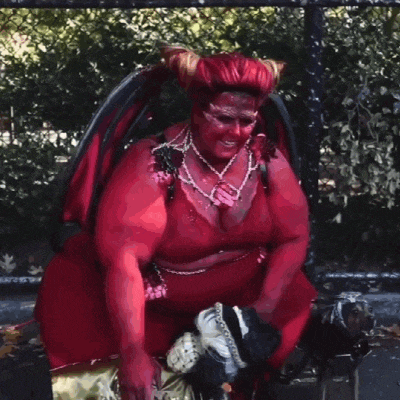 a woman dressed as a devil is sitting on a bench with a dog