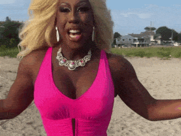 a woman in a pink tank top and necklace is standing on a sandy beach