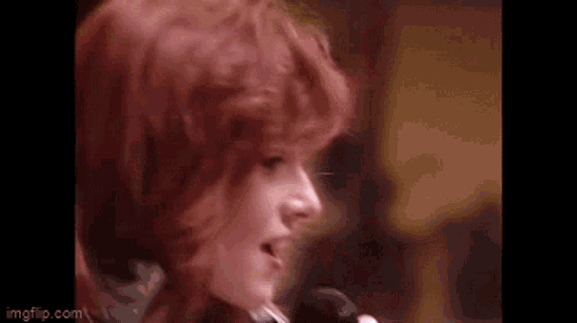 a woman with red hair is singing into a microphone in a close up .