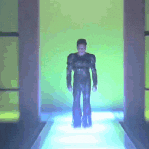 a man in a black suit is walking down a blue runway