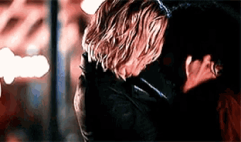 a man and woman are hugging each other in a dark room . the woman is wearing a mask .