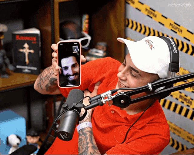 a man wearing headphones and a red shirt holds up a cell phone