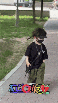 a young boy wearing a mask and a hat is walking down a sidewalk with the word alone in the background
