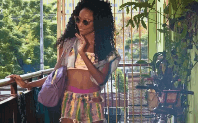 a woman in a crop top and shorts is standing on a balcony talking on a cell phone