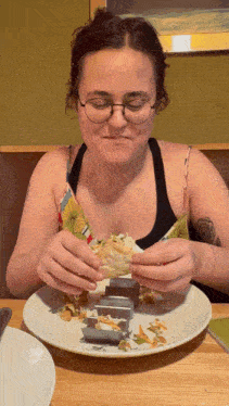 a woman wearing glasses is eating a sandwich on a white plate