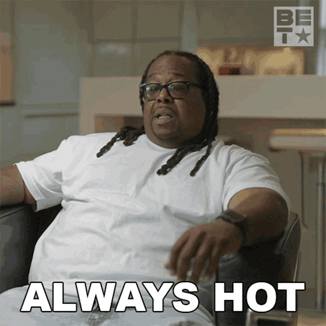 a man with dreadlocks is sitting in a chair with the words " always hot " above him