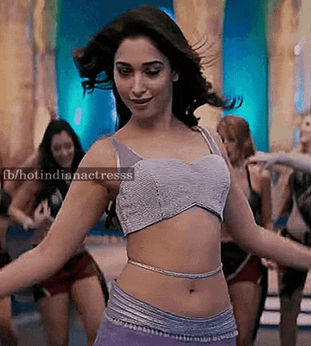 a woman in a crop top and purple pants is dancing in front of a crowd .