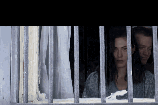 a woman is behind bars looking out a window
