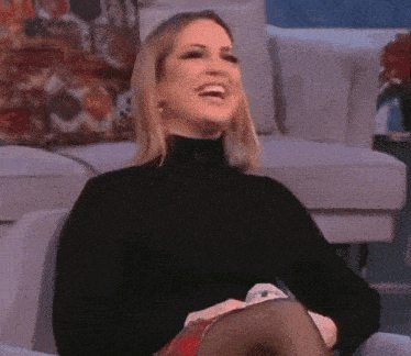 a woman wearing a black turtleneck is laughing while sitting on a couch