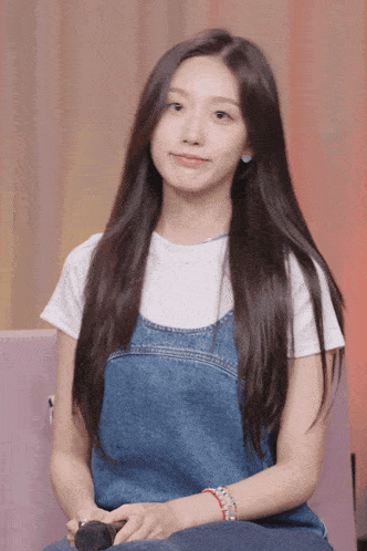 a woman wearing a white shirt and denim overalls is sitting on a couch