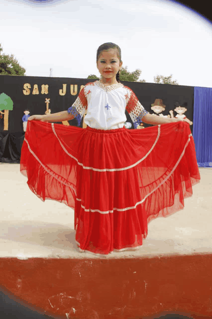 a little girl in a red skirt stands in front of a sign that says san juarez