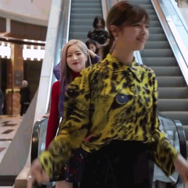 a woman in a yellow shirt is walking down an escalator with another woman