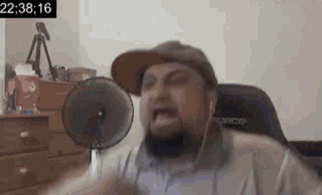 a man with a beard and hat is sitting in front of a microphone and making a funny face .