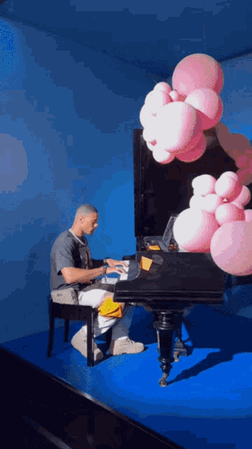 a man sits at a piano with pink balloons behind him