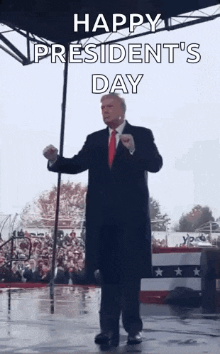 a man in a suit and tie is standing in front of a crowd and holding a flag .