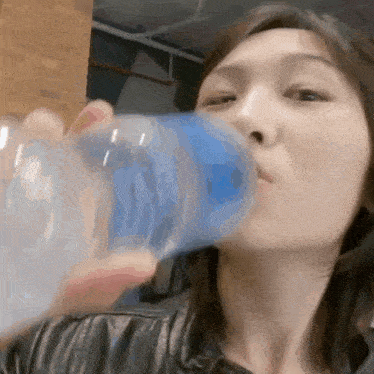 a woman is drinking water from a blue glass