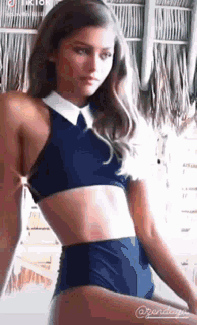 a woman in a bikini top and high waisted bottoms is standing in front of a palm tree .