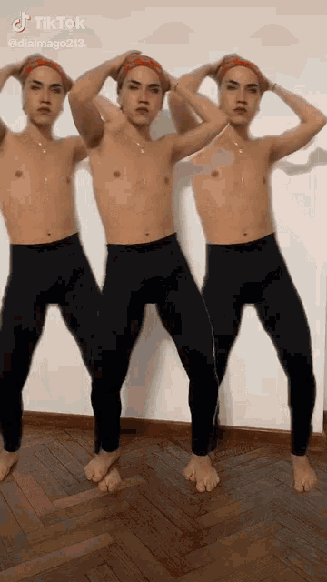 three men without shirts are standing next to each other on a wooden floor .
